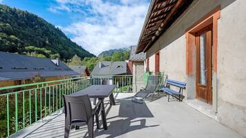 A balcony with a table and chairs, a bench, and a view of a mountain.
