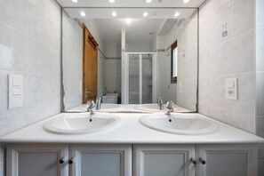 Une salle de bain moderne avec deux lavabos, une douche et un miroir.