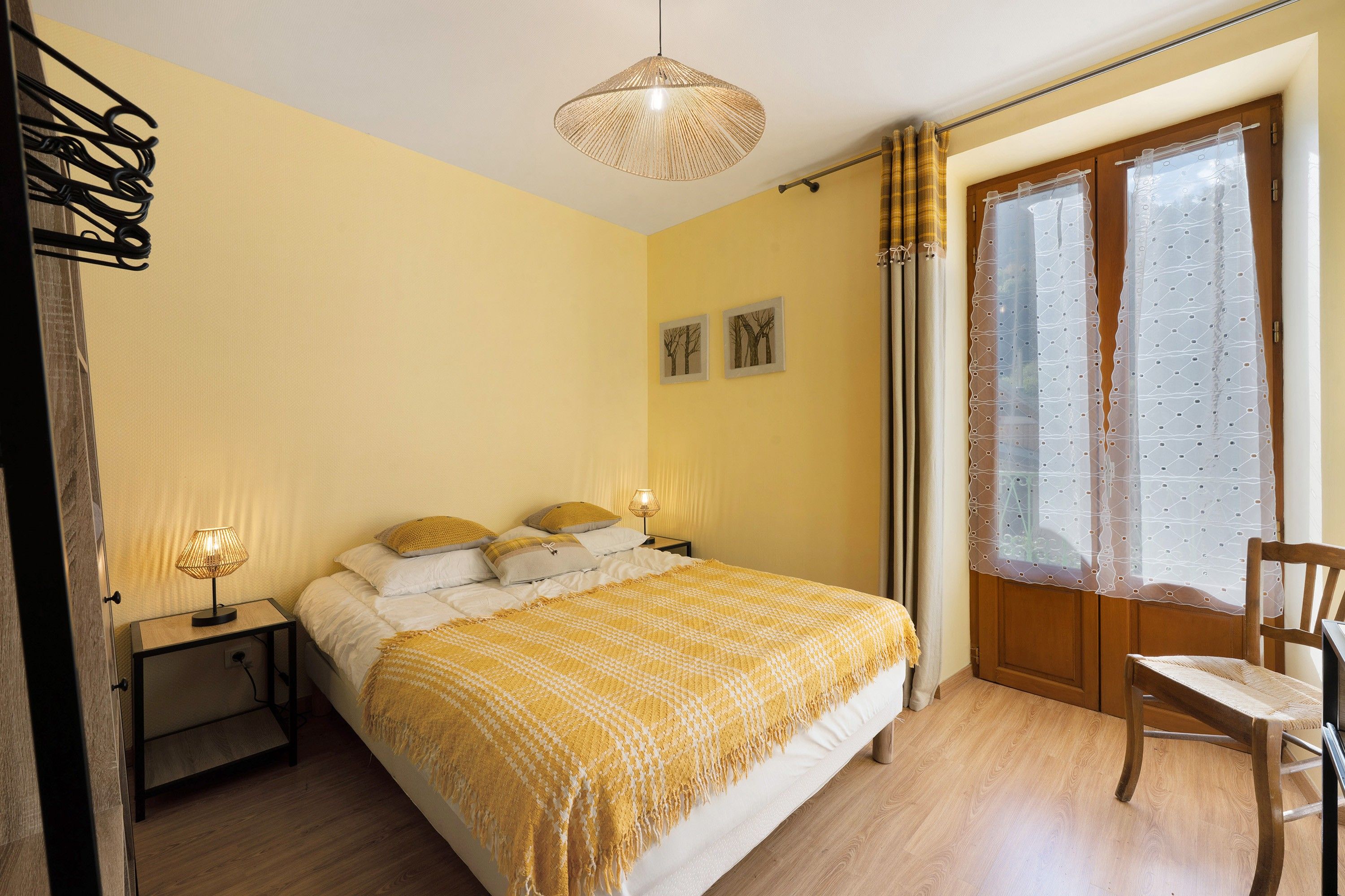Un dormitorio con cama, lámparas de noche, una silla, un ventanal con cortinas y decoración en la pared.