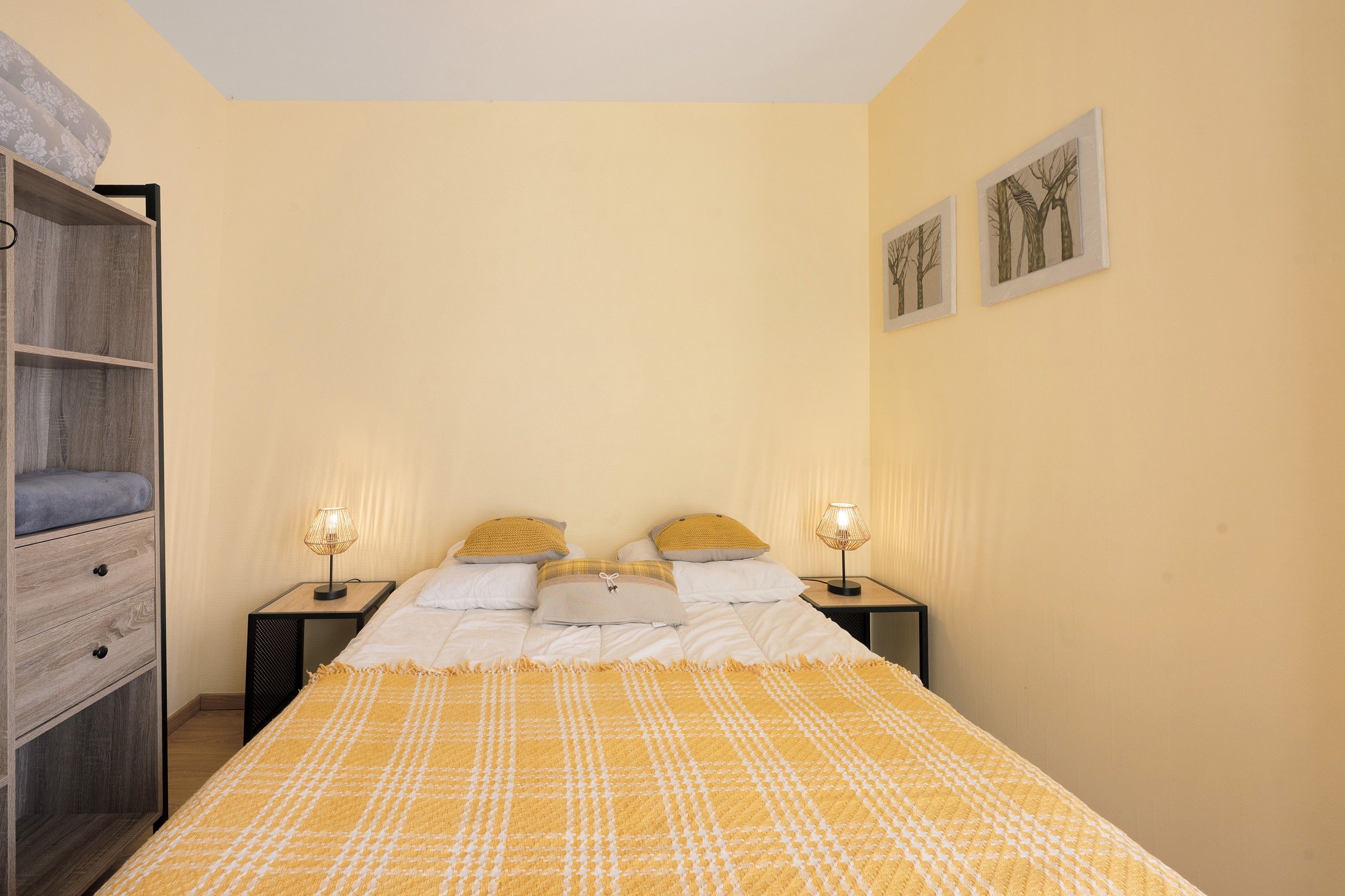 Un dormitorio con cama, dos mesitas de noche con lámparas, un armario y dos cuadros en la pared.