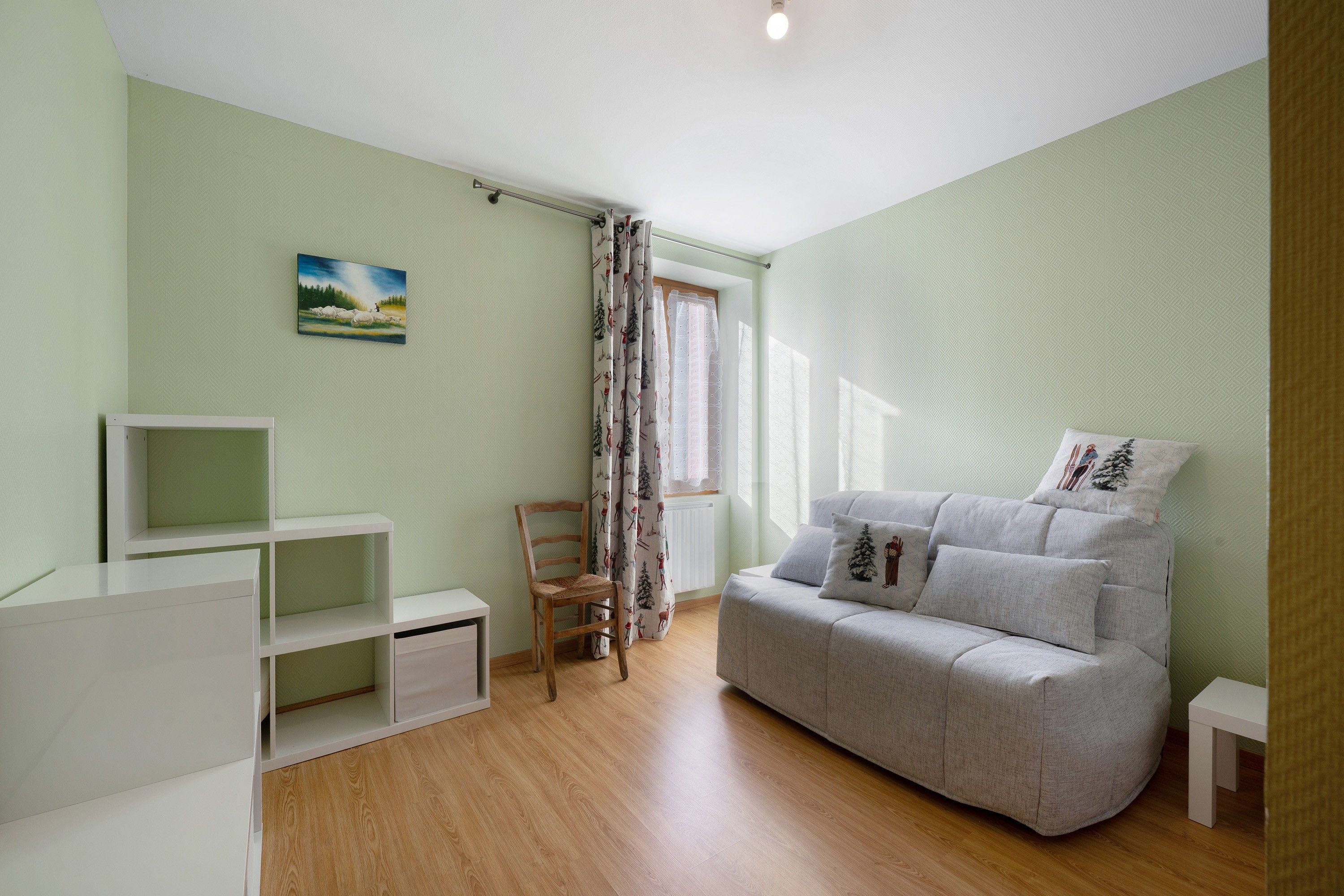 Una habitación con un sofá gris, una silla de madera, un mueble blanco para televisión y un cuadro en la pared.