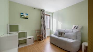 Una habitación con un sofá gris, una silla de madera, un mueble blanco para televisión y un cuadro en la pared.