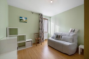 Una habitación con un sofá gris, una silla de madera, un mueble blanco para televisión y un cuadro en la pared.