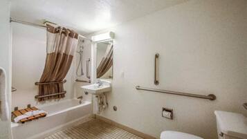 A standard bathroom with a bathtub, sink, toilet, and grab bars.