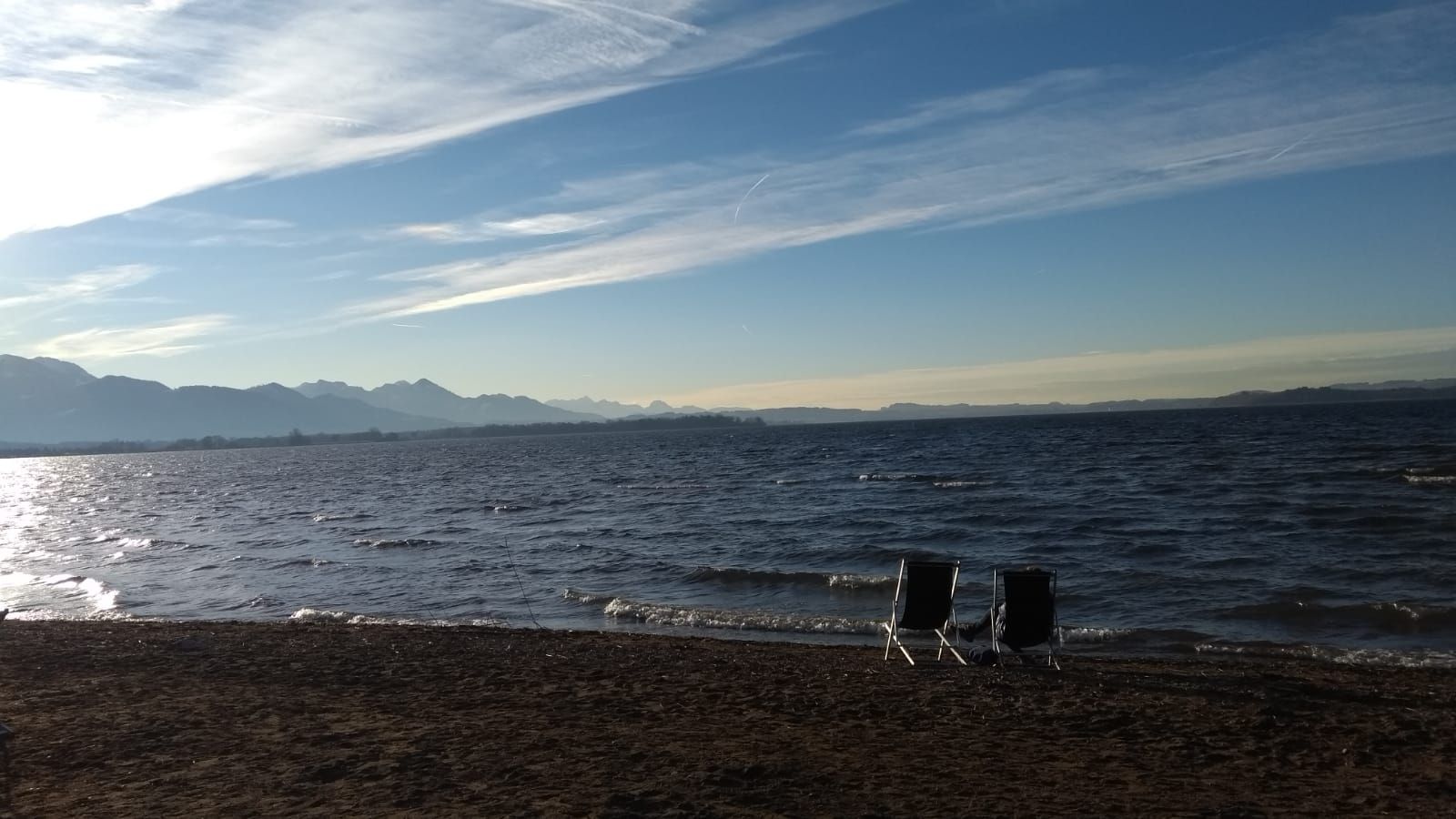 Een strand met twee strandstoelen gericht op de oceaan, een heldere lucht en verafgelegen bergen.