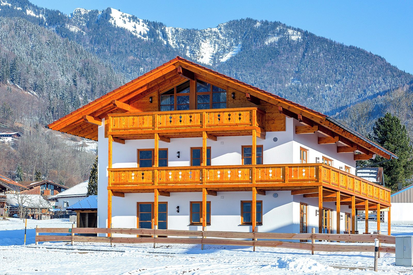 Un chalet en bois à plusieurs étages, doté de balcons, qui se dresse sur fond de montagnes enneigées.
