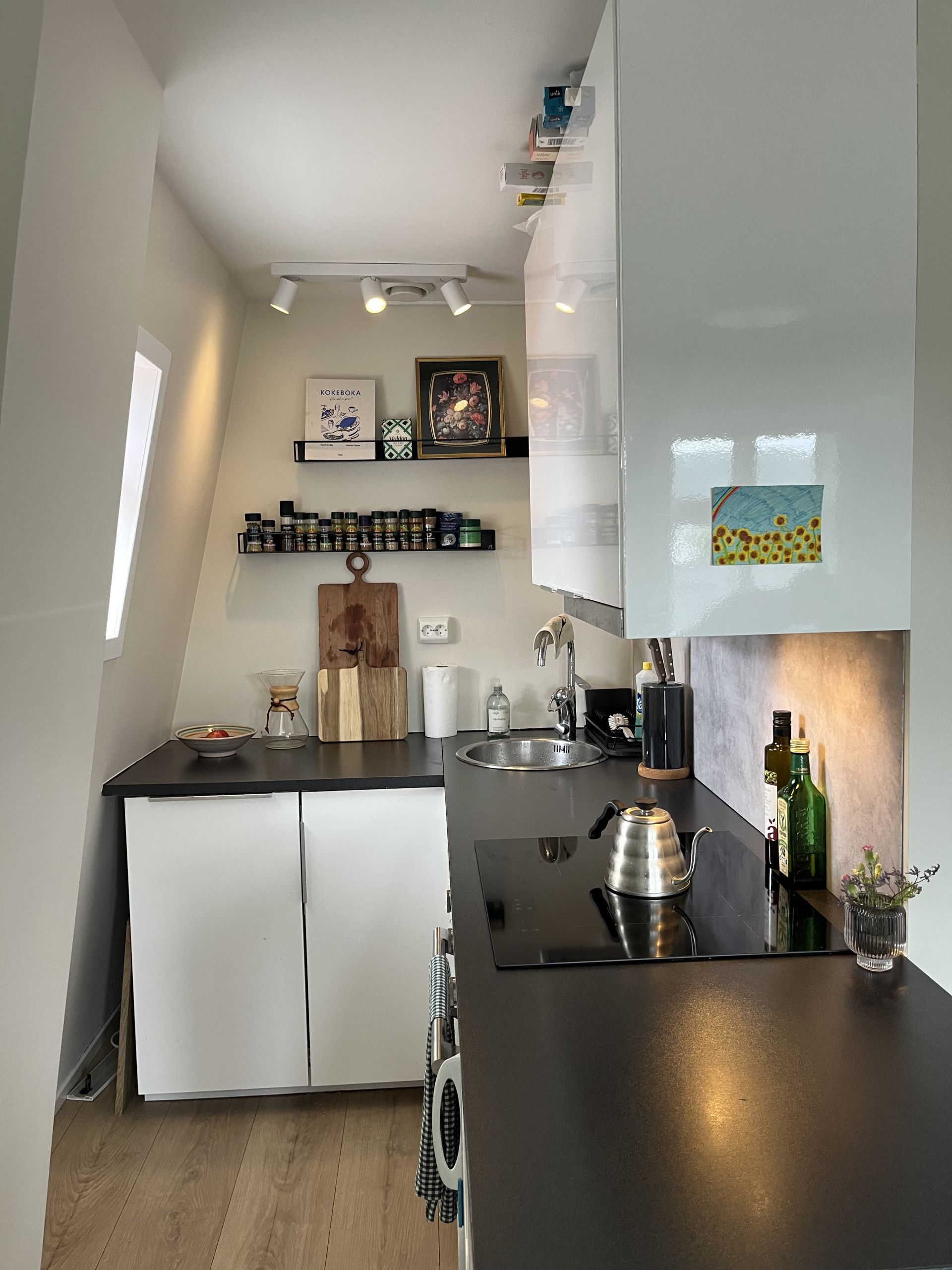 A modern kitchen with a built-in oven, a sink, and a coffee machine. There are cabinets, a countertop, and a window providing natural light.