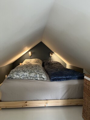 Una camera da letto in stile loft con soffitto spiovente, due luci a parete e un letto con biancheria a fiori e tinta unita.