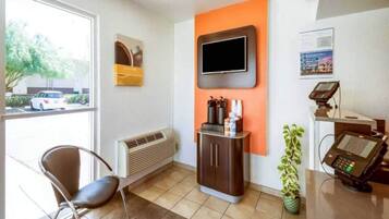 Un espace d’accueil comprenant une chaise, un téléviseur fixé au mur, une plante et un terminal de paiement.