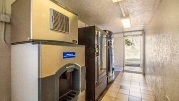 A hallway with a vending machine, a trash bin, and a door leading outside.