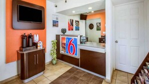 Zona de recepción con mostrador, televisor montado en la pared, planta y una puerta.