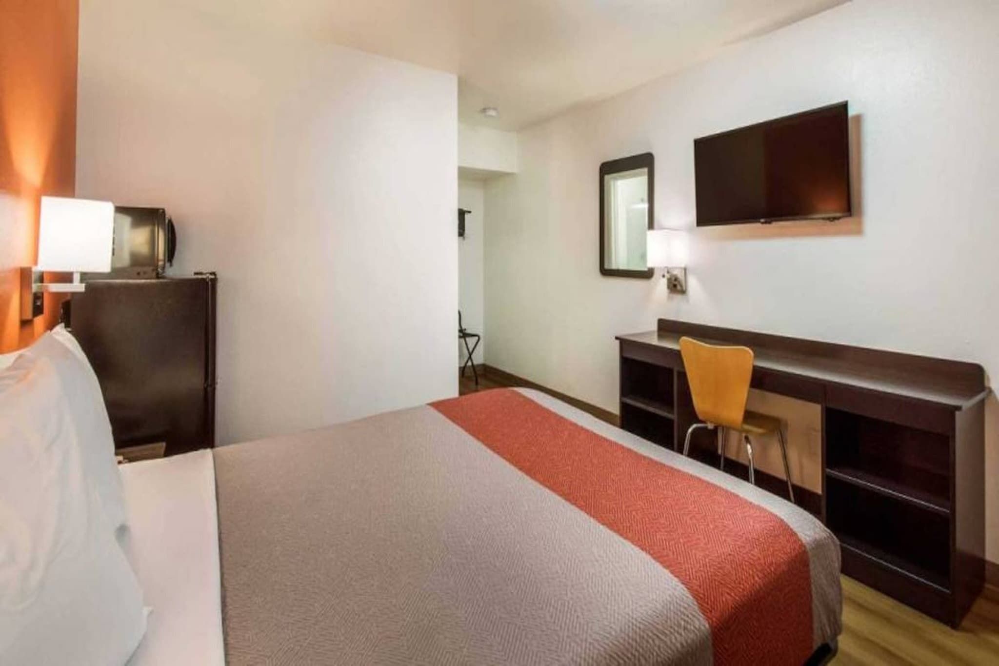 Ein Hotelzimmer mit Bett, Schreibtisch, Stuhl, Fernseher und Spiegel.