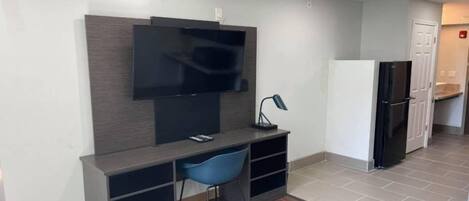 A modern kitchen with a built-in refrigerator, a flat-screen TV mounted on the wall, and a blue chair at a dark-colored desk.
