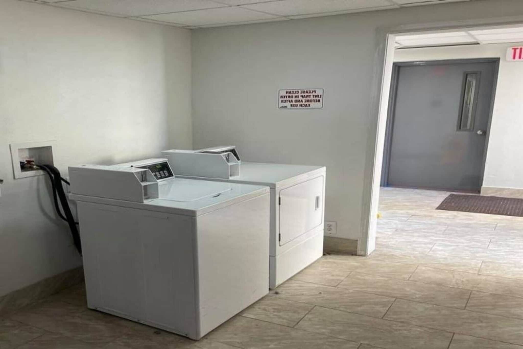 A laundry room with two white washers and dryers, a sign on the wall, and a door leading to another room.