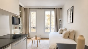 A modern hotel room with a bed, a desk, a TV, and a balcony with curtains. - Studio cosy au cœur du 10 arrondissement (Paris)