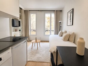Una habitación de hotel moderna con cama, escritorio, televisión y balcón con cortinas.