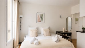 A hotel room with a bed, bedside table, mirror, and a window with curtains. - Studio cosy au cœur du 10 arrondissement (Paris)