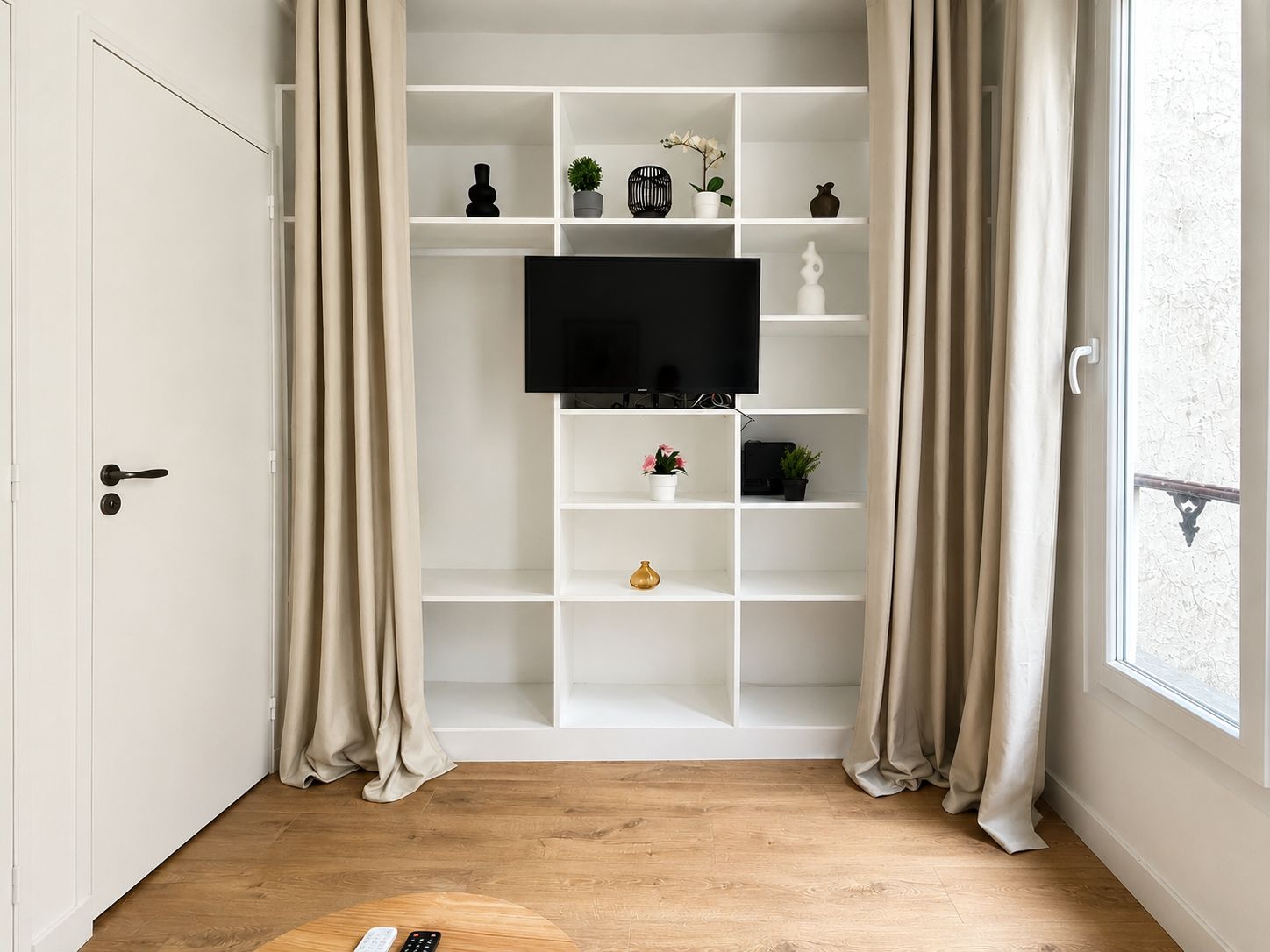 A room with a white built-in TV shelf, wooden flooring, and a door with a handle.