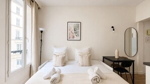 A hotel room with a bed, a desk, a chair, a lamp, and a window with curtains. - Studio cosy au cœur du 10 arrondissement (Paris)