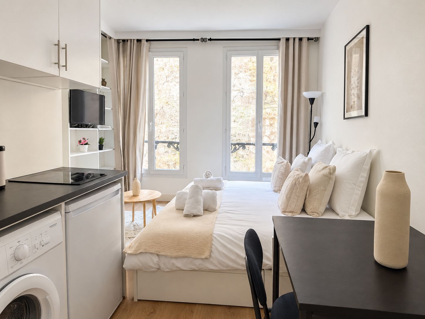 A compact hotel room with a bed, a desk, a washing machine, and a TV.