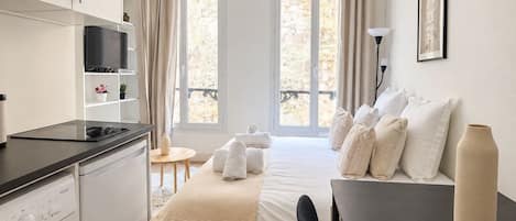 Une chambre d’hôtel de taille réduite, équipée d’un lit, d’un bureau, d’une machine à laver et d’un téléviseur.
