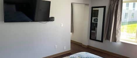 A room with a flat-screen TV mounted on the wall, a patterned rug on the floor, and a window with curtains.
