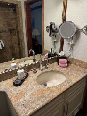 Casa de banho com bancada de granito, duas pias, espelho e porta-toalhas.