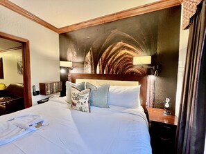 Quarto de hotel com uma cama grande, cabeceira com mural de teto catedral e mesas de cabeceira com luminárias.