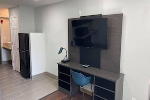 A modern kitchen with a built-in refrigerator, a flat-screen TV mounted on the wall, and a small desk with a chair. - 1 Queen Bed | Non-Smoking, Sofa-Bed (Peoria IL)