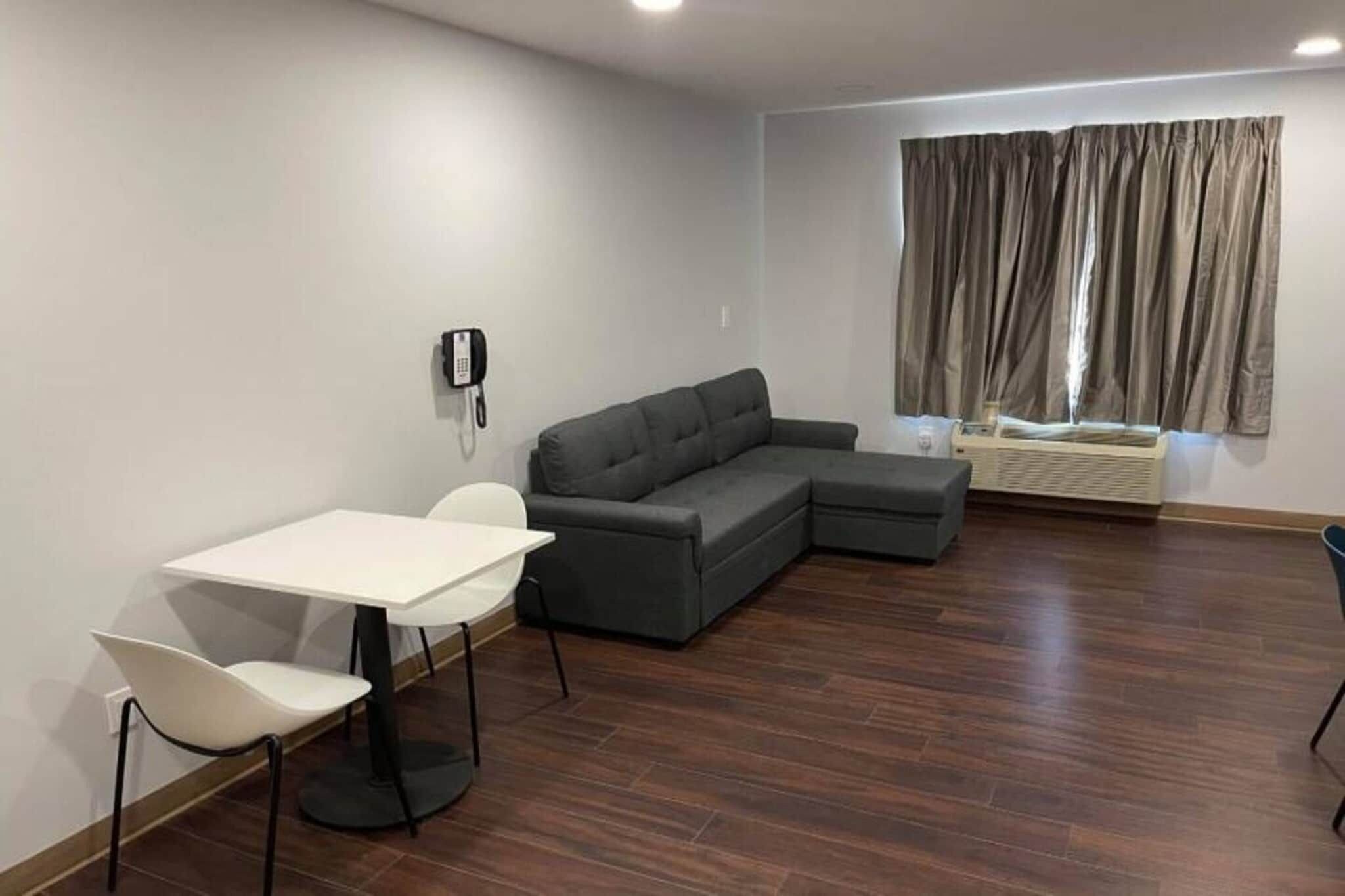 Una sala moderna con un sofá modular, una mesa de comedor con sillas, un teléfono en la pared y una ventana con cortinas.