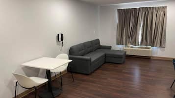 Una sala moderna con un sofá modular, una mesa de comedor con sillas, un teléfono en la pared y una ventana con cortinas.