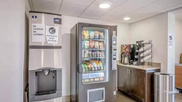 Máquina expendedora con snacks y bebidas frías, una máquina de café y un dispensador de agua en un entorno comercial.