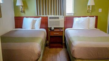A hotel room with two beds, a nightstand, an air conditioning unit, and a window with curtains.