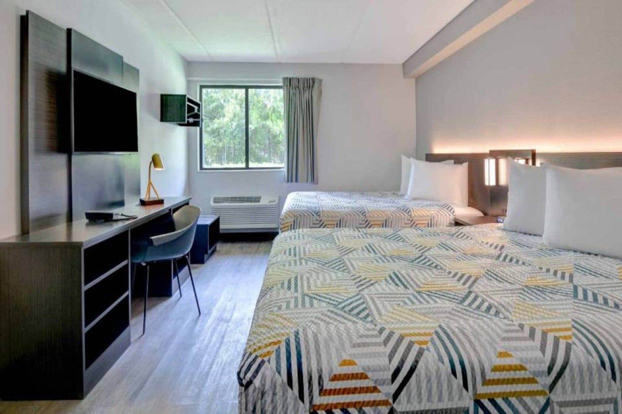 Quarto de hotel com cama, escrivaninha, cadeira, televisão e janela com cortinas.