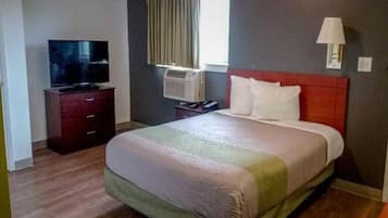 A hotel room with a bed, a television, an air conditioning unit, and a window with curtains.