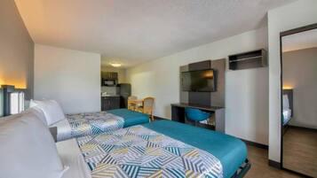 A hotel room with two beds, a desk, a television, and a kitchenette.