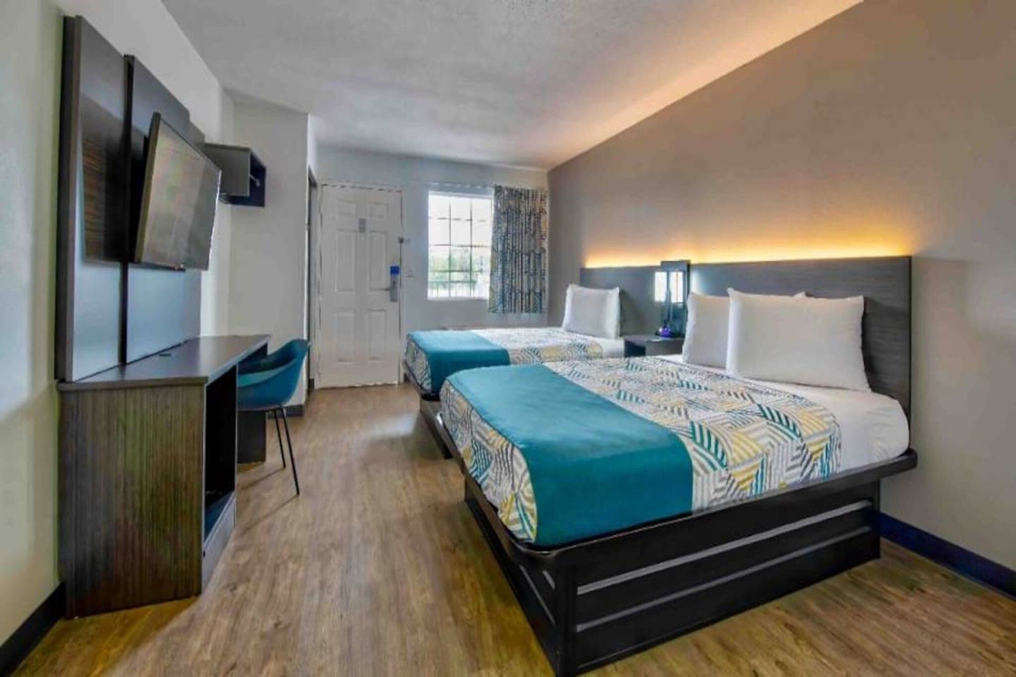 A hotel room with two beds, a desk, a TV, and a window.