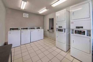 A laundry room with multiple washing machines and dryers, a tiled floor, and a sign on the wall. - 2 Full Beds | Non-Smoking (Pascagoula)
