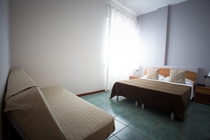 Quarto de hotel com cama, cadeira, mesa de cabeceira e janela com cortinas.