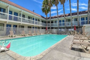 A hotel with a pool area, multiple balconies, and palm trees. - 1 Queen Bed | ADA/Tub (Pomona CA)