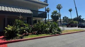 Un hotel con techo de tejas, balcón y estacionamiento con palmeras.