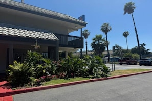 A hotel with a tiled roof, a balcony, and a parking lot with palm trees. - 1 Queen Bed | ADA/Tub (Pomona CA)