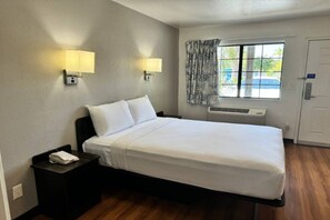 Hotelkamer met een enkel bed, nachtlampjes, een raam met gordijnen, een airconditioning en een deur met slot.