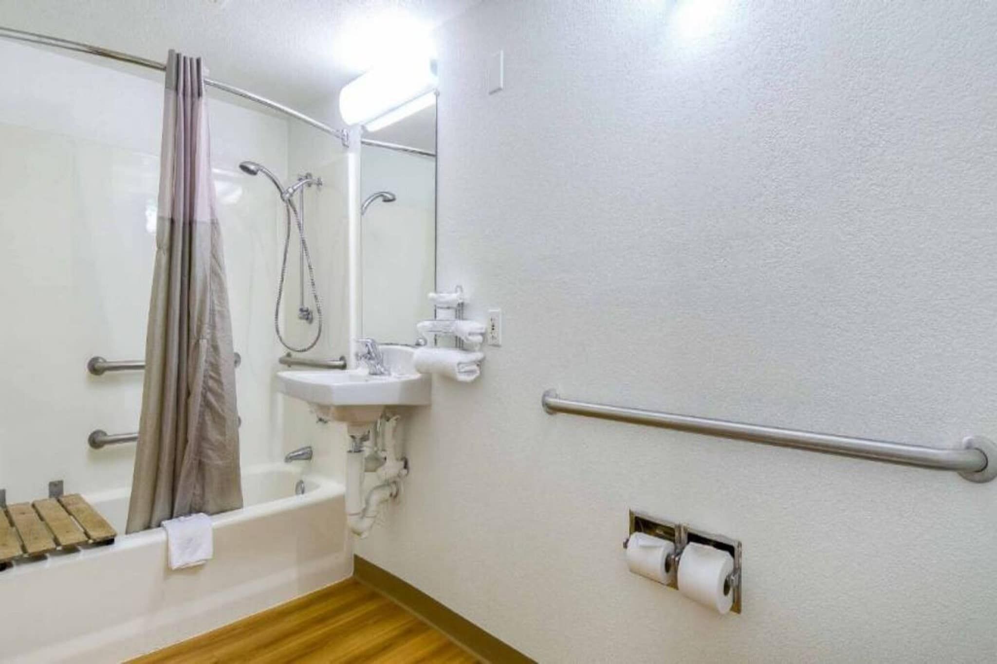 Een badkamer met een bad, een wastafel, een douche, een spiegel en een toiletrolhouder.