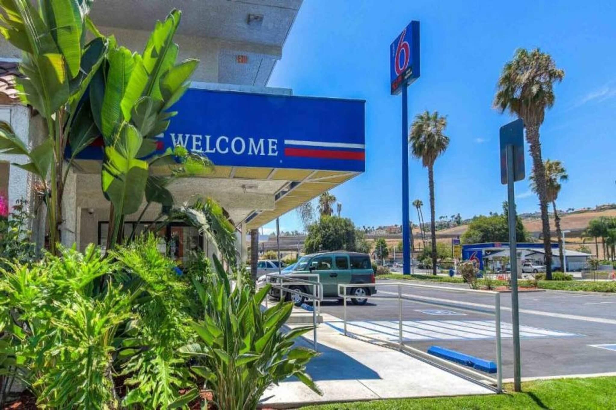Eine Tankstelle mit einem 'Welcome'-Schild, Palmen und blauem Himmel.