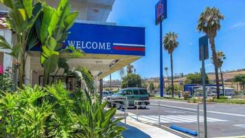 Eine Tankstelle mit einem 'Welcome'-Schild, Palmen und blauem Himmel.