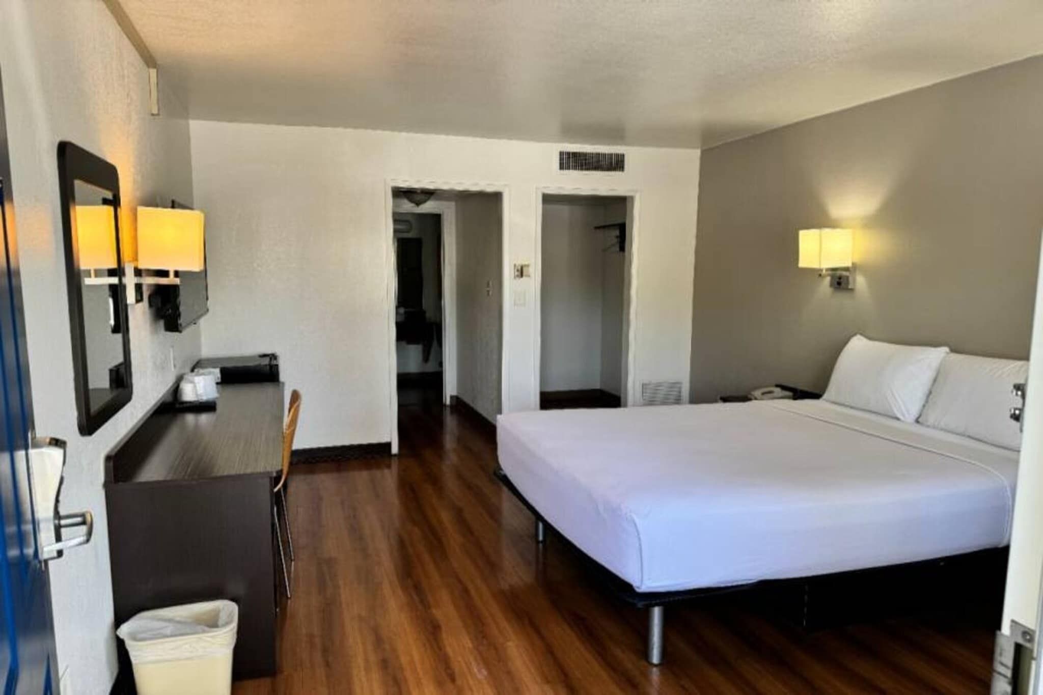 A hotel room with a bed, a desk, a chair, and a trash bin.
