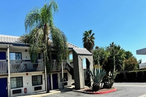 A multi-story building with balconies, a palm tree, and a pineapple plant in the foreground. - 1 Queen bed | Los Angeles (Pomona CA)
