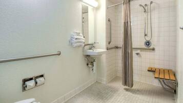 Een badkamer met een handgreep, wastafel, douche en een bankje.