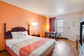 Una habitación de hotel con cama, mesita de noche, lámpara, escritorio, silla y televisor.